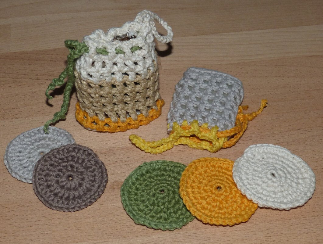 Gehäkeltes Set aus runden Scheiben in Gelb, Grün, Weiß und Braun mit zwei kleinen Zugbeuteln auf Holzuntergrund