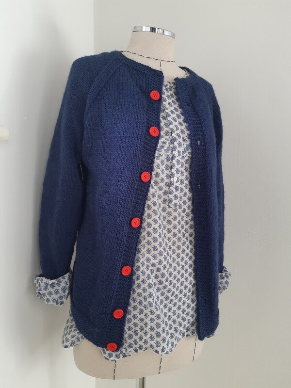 Navy knitted women's cardigan with red buttons on a dress form over a patterned blouse