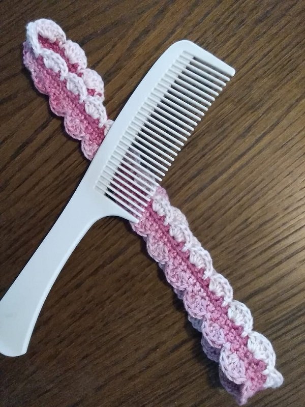 Zweifarbiges rosa gehäkeltes Stirnband mit wellenförmigem Muschelmuster, um einen weißen Haarkamm gelegt auf einem Holztisch.