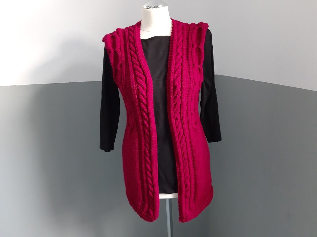 Lange ärmellose Strickweste in Magenta mit Zopfmuster auf Mannequin über schwarzem Langarmshirt