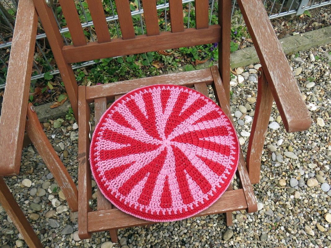 Rundes gehäkeltes Sitzkissen in Rot und Pink auf einem Holzstuhl