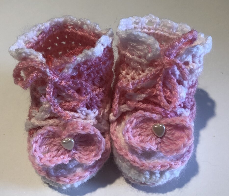 Frontalaufnahme gehäkelter rosa-weißer Babyschuhe mit Schnürung und Herzknöpfen