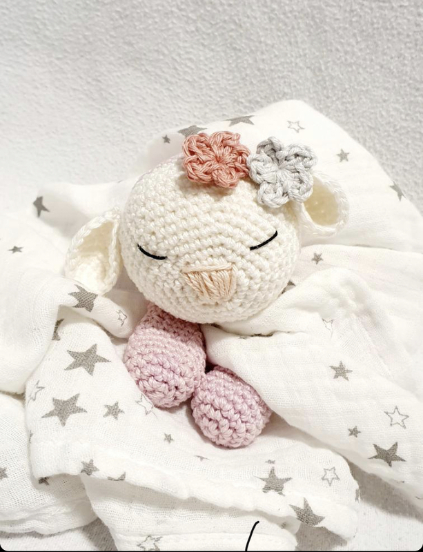 Handgehäkeltes Babyschaf mit geschlossenen Augen und Blumenapplikationen auf Sternenmulltuch