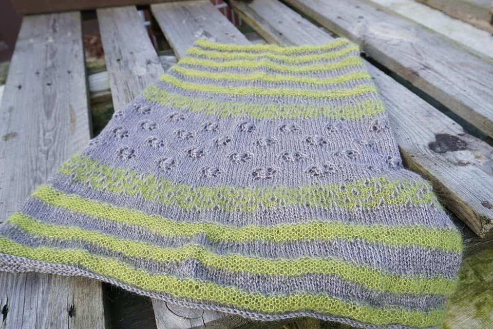 Gestrickter Schlauchschal in Grau und Lindgrün mit Streifen und Lochmuster auf Holzlatten.