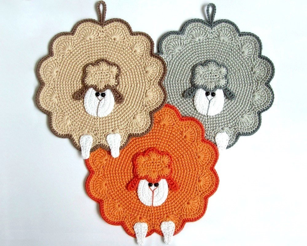 Drei gehäkelte Topflappen in Schafform in Beige, Grau und Orange mit Aufhängeschlaufen.