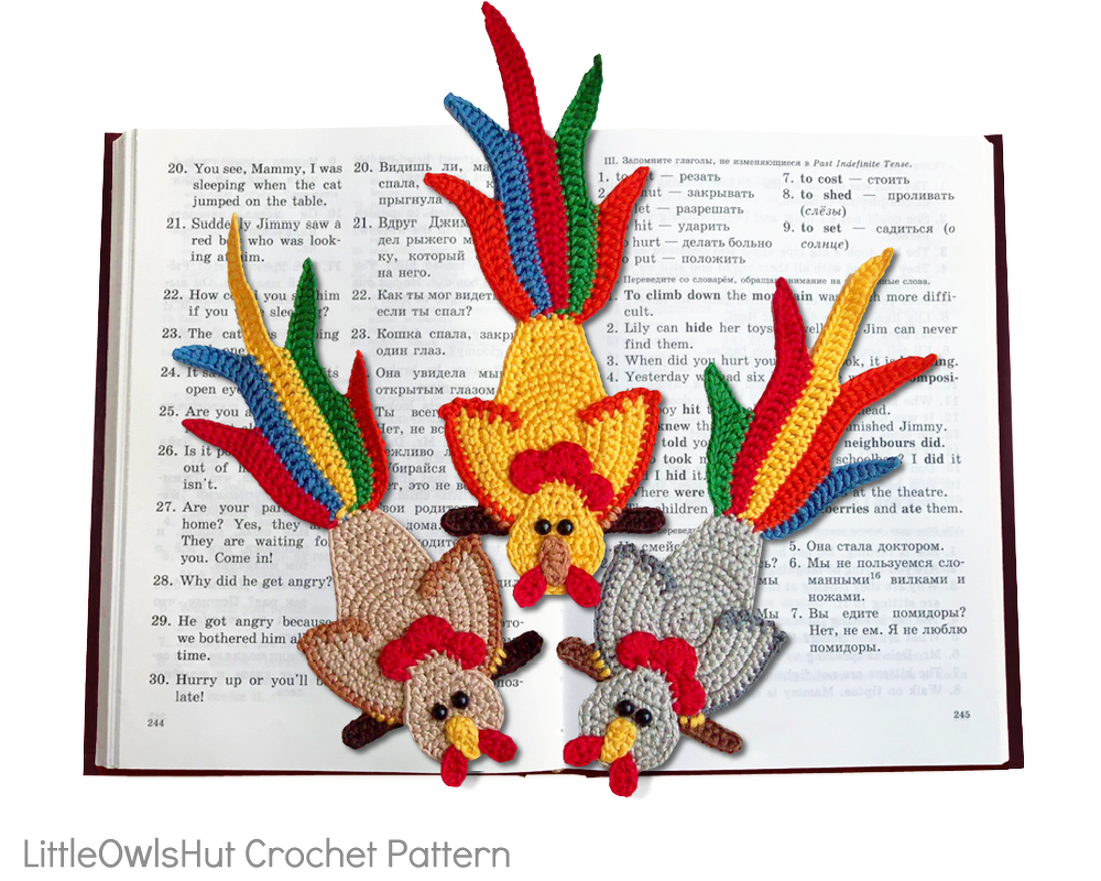 Drei gehäkelte Hähnchen-Lesezeichen mit bunten Schwänzen auf einem aufgeschlagenen Buch