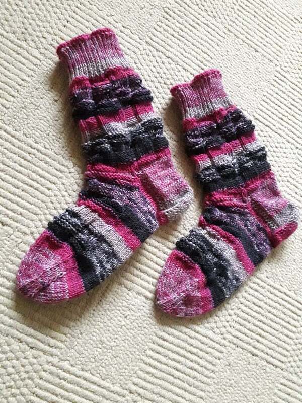Paar handgestrickte Ringelsocken in Pink, Rosa und Grau mit Noppenmuster auf hellem Untergrund