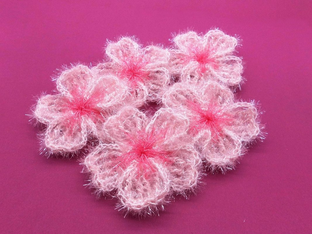 Fünf kleine flauschige rosa Häkelblüten mit dunklerer Mitte auf kräftigem Pink