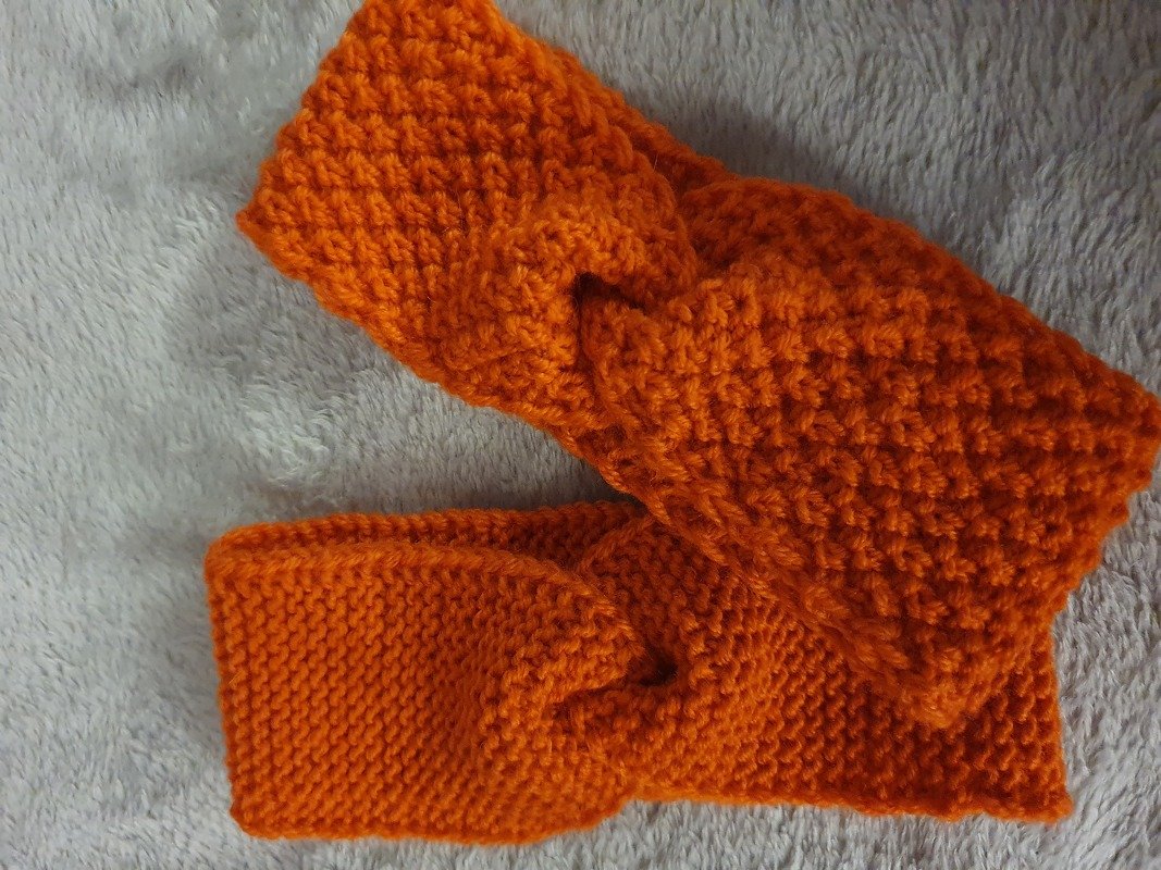 Gestricktes Baby-Stirnband orange mit Knoten auf hellgrauer Decke