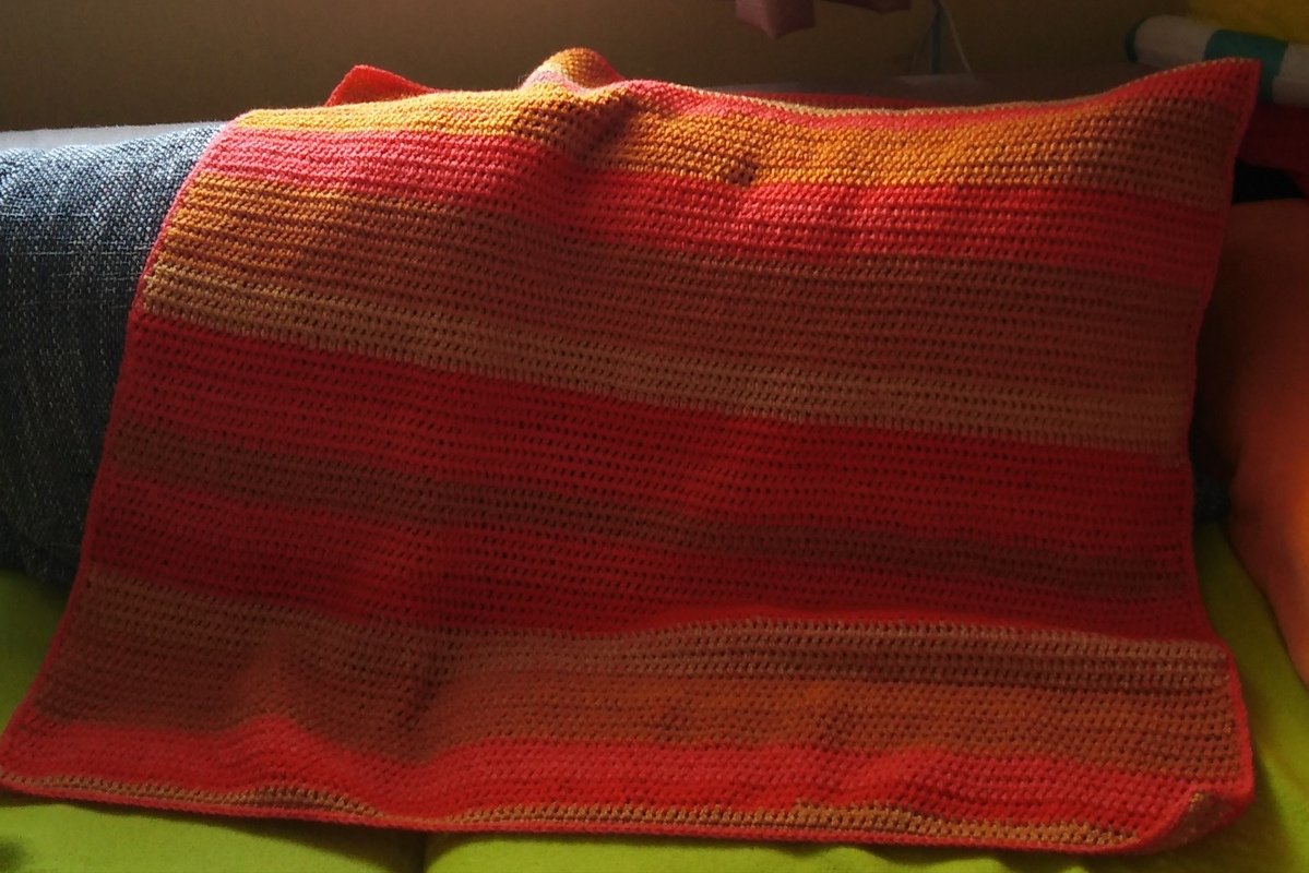 Gehäkelte Decke mit roten und orangen Streifen über einem Sofa drapiert
