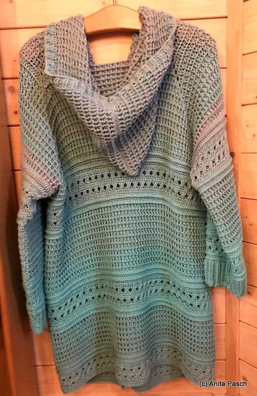 Lange gehäkelte Damen-Kapuzenjacke in Mintgrün mit Loch- und Strukturmustern an einem Holzbügel