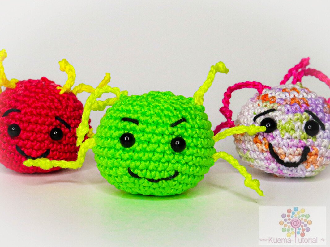 Drei schnell gehäkelte Amigurumi-Kugeln in Rot, Grün und Pastell mit gestickten Gesichtern