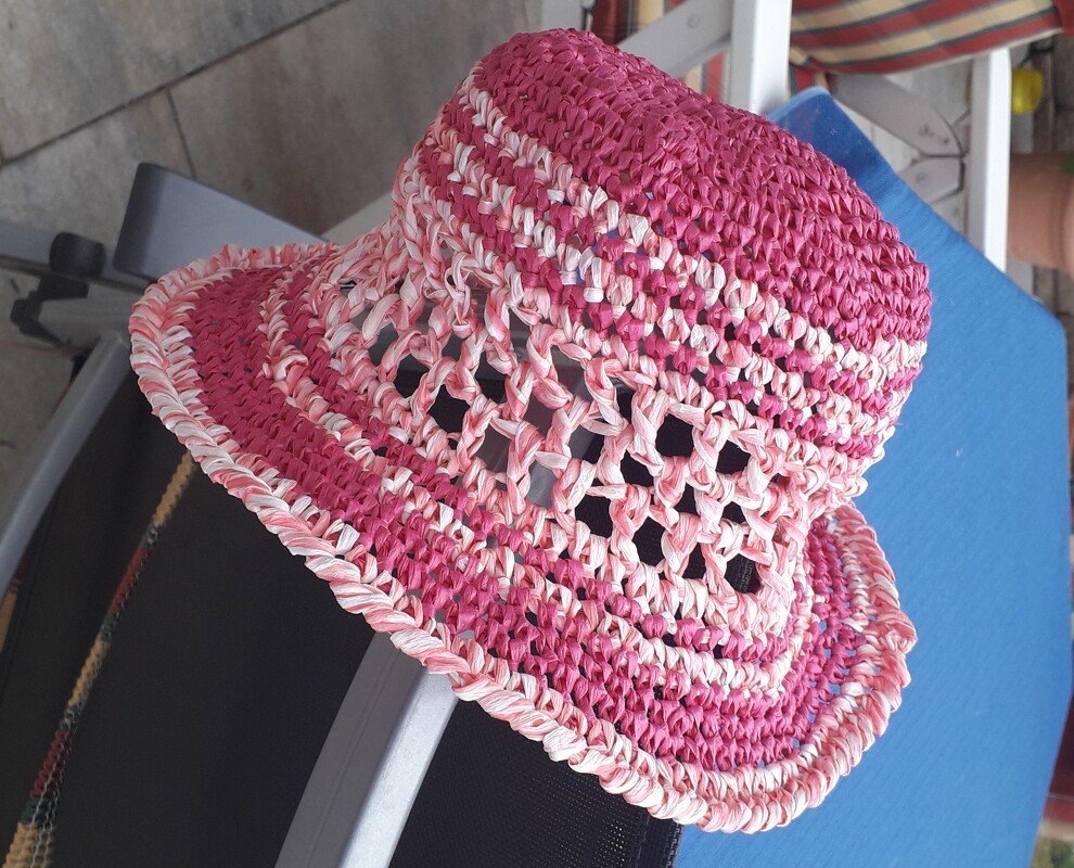 Gehäkelter Kinderhut in Pink und Weiß mit Lochmuster auf blauer Oberfläche