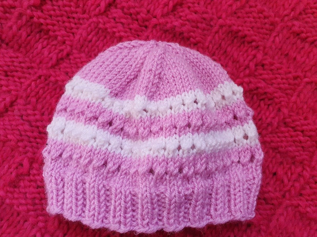 Hellrosa Babymütze mit weißen Streifen und Rippenbündchen auf pinkem Hintergrund