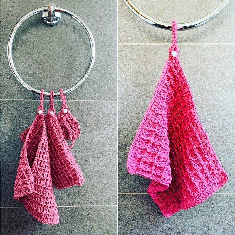 Gehäkelte rosa Handtücher mit Schlaufen und weißen Druckknöpfen an einem Metallring vor grauen Fliesen