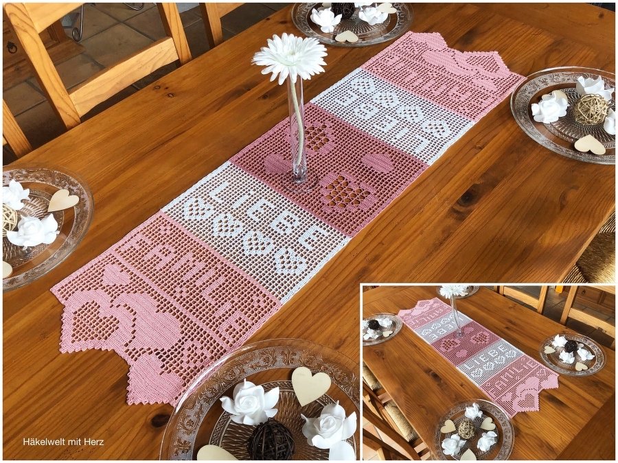 Rosa-weißer gehäkelter Tischläufer mit den Worten LIEBE und FAMILIE und Herzmotiven auf einem Holztisch