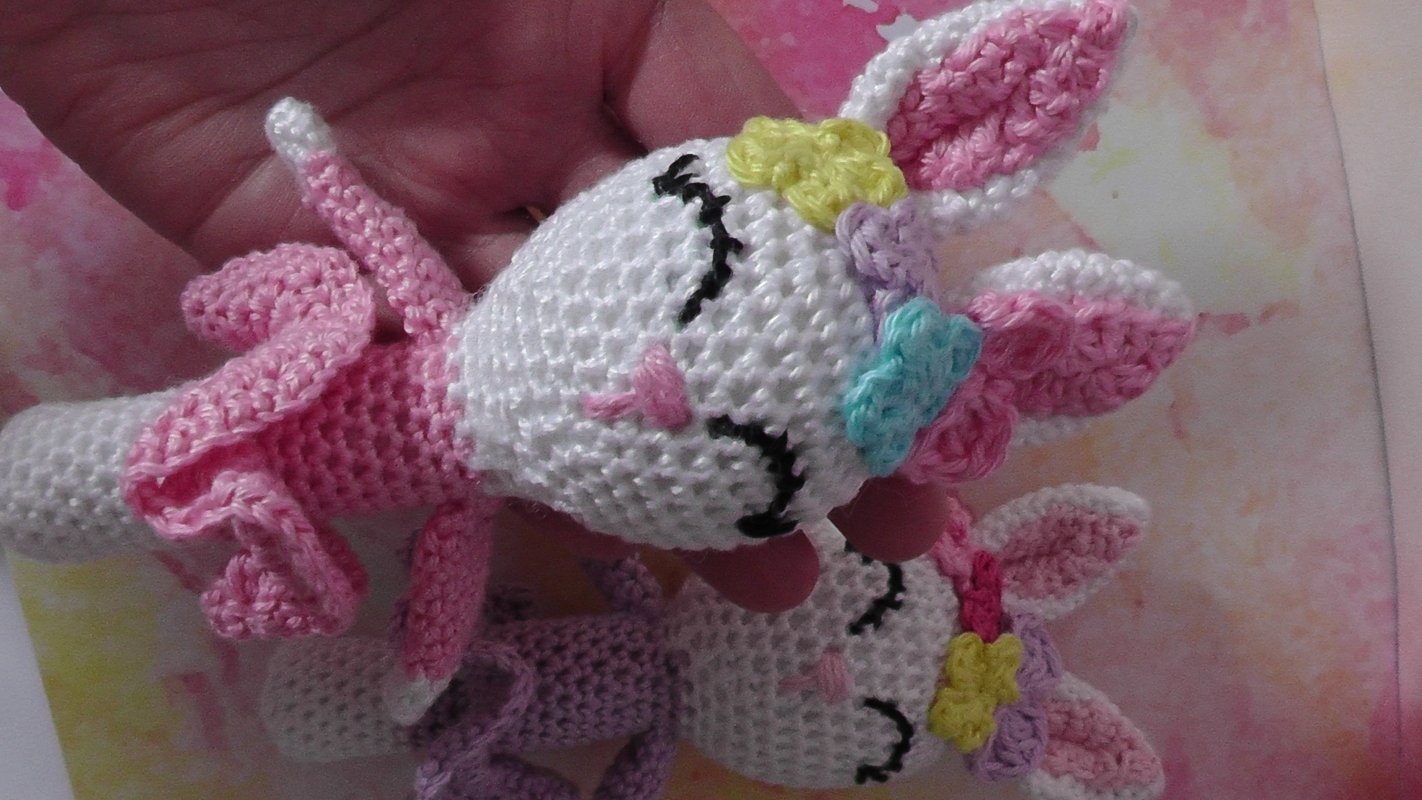 Two crocheted amigurumi bunny handrings in pink and purple with flower details, shown held in a hand.