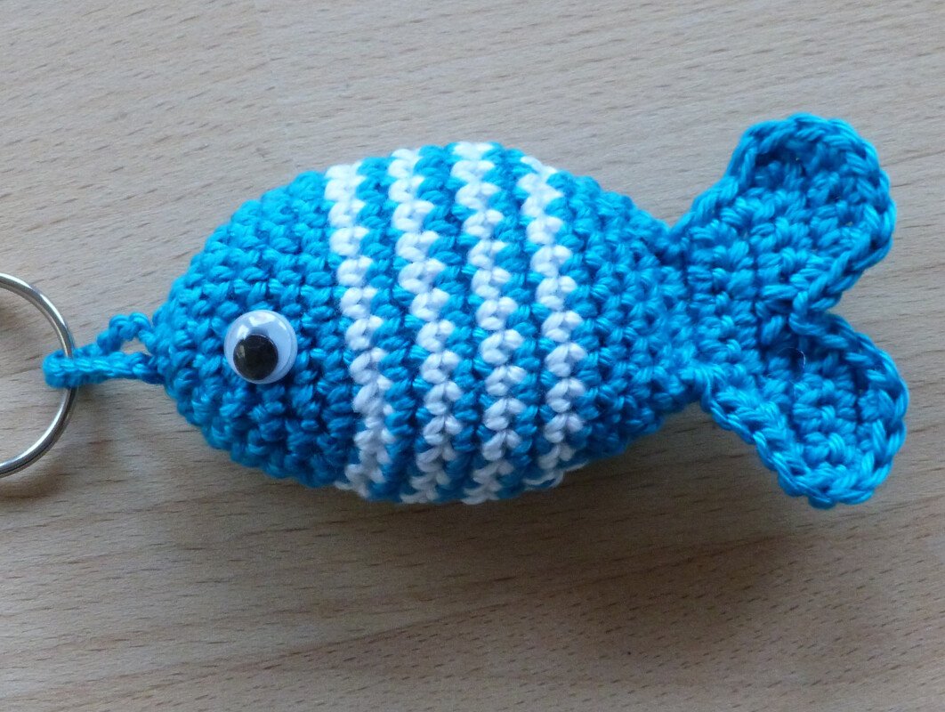 Gehäkelter blau-weiß gestreifter Fisch-Schlüsselanhänger mit Wackelauge auf hellem Holz