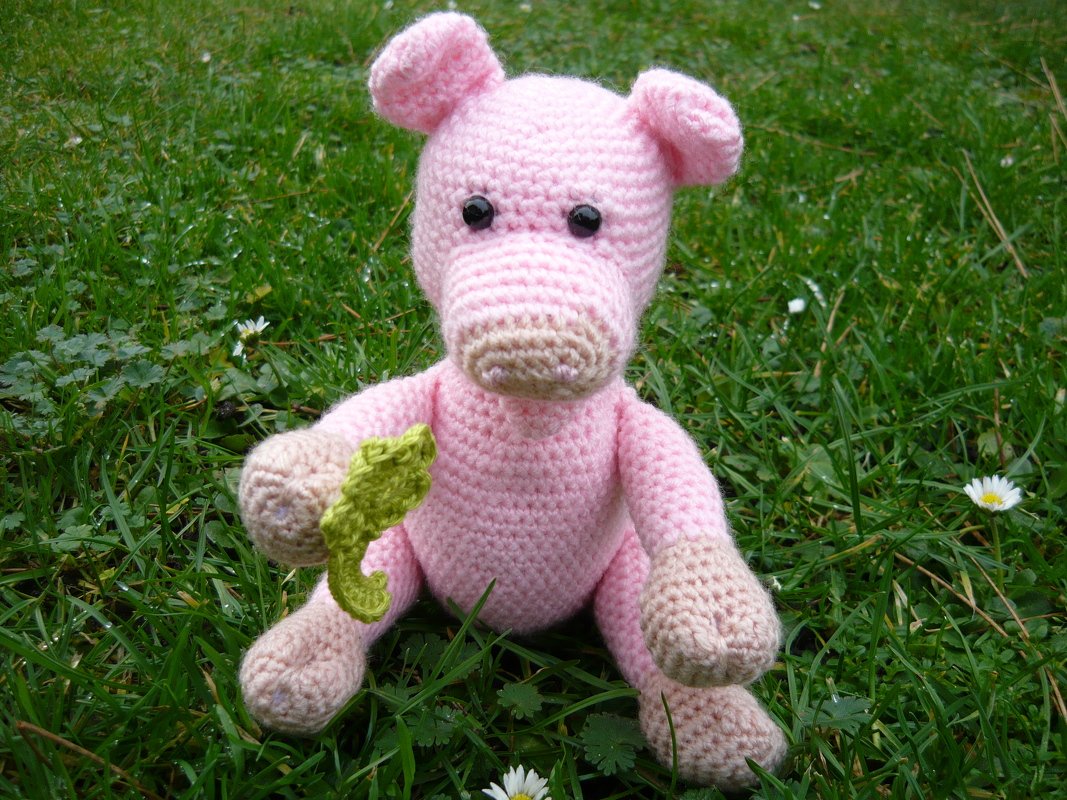 rosa gehäkeltes Amigurumi‑Schwein mit grünem Kleeblatt im Gras