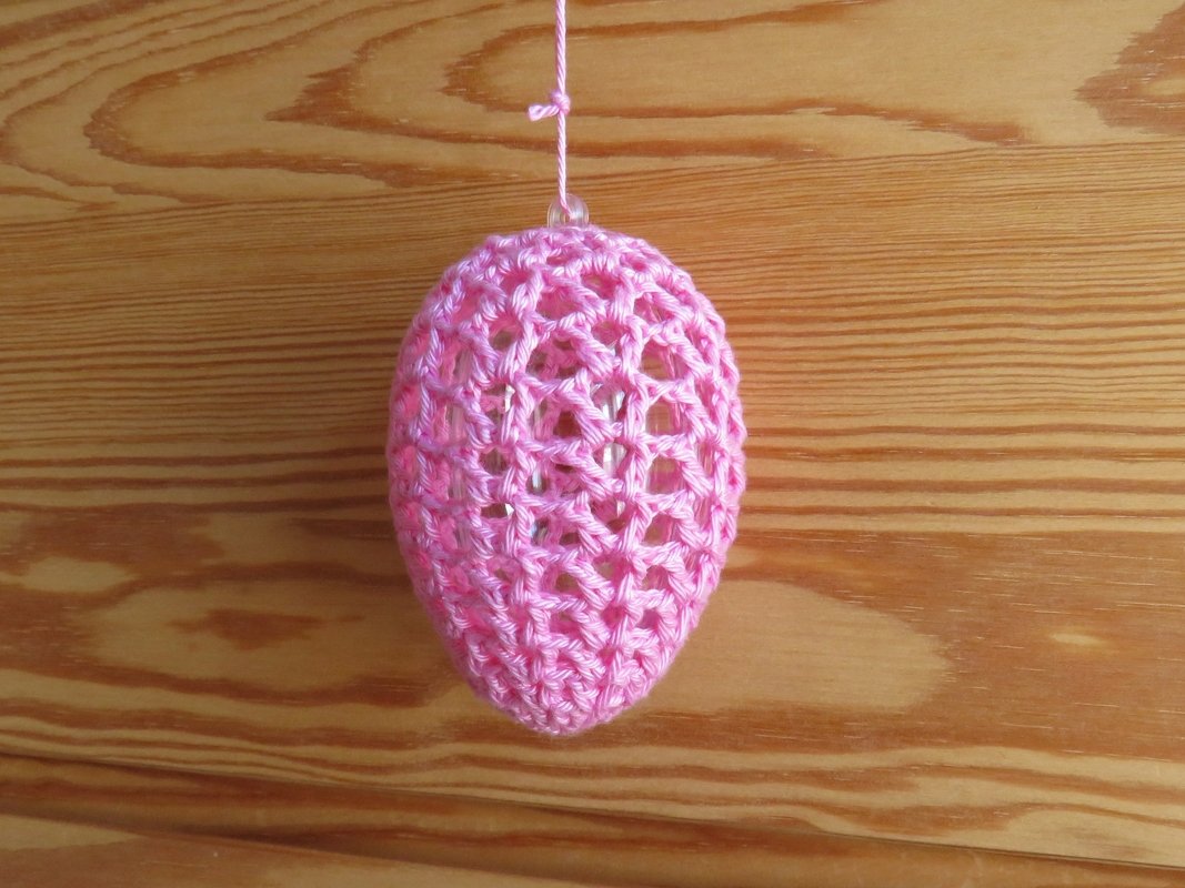 Schlanke rosa gehäkelte Eihülle mit offenem Maschenmuster an Schnur