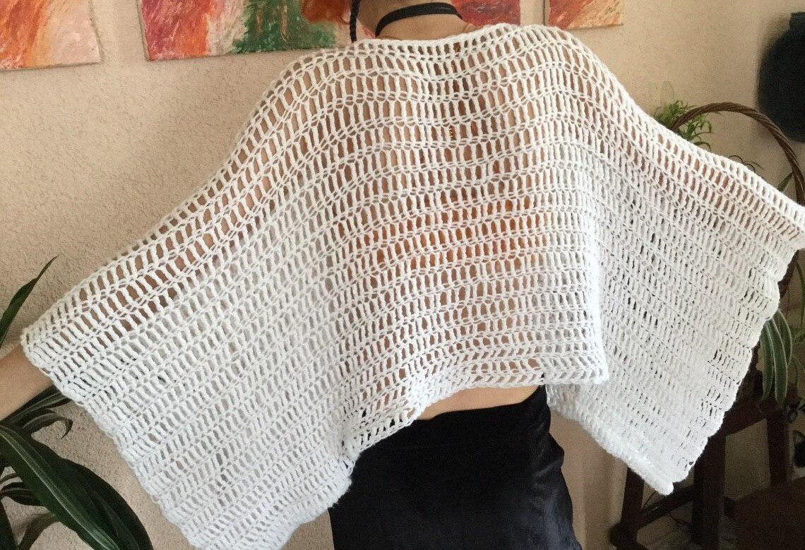 Rückansicht einer Person in einem weißen, locker gehäkelten Poncho mit transparentem Lochmuster.