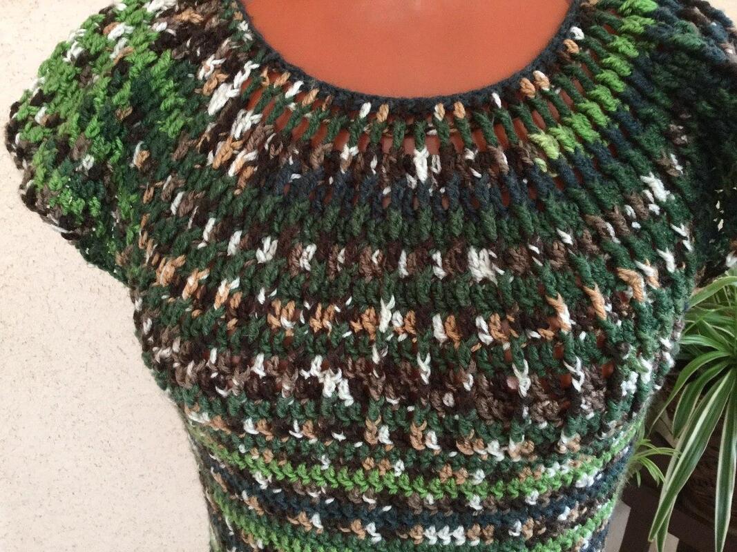 Nahaufnahme eines gehäkelten Damenkleids in Grün-, Braun- und Cremetönen mit Rundhalsausschnitt