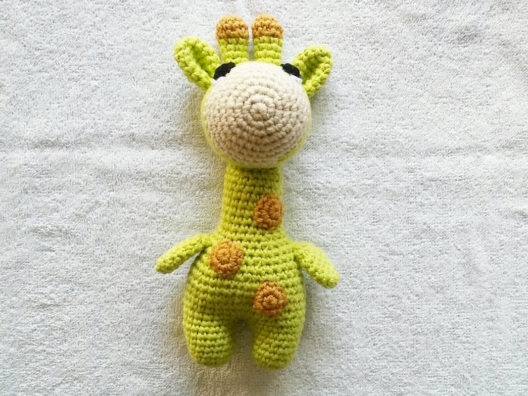 Light green and cream crocheted giraffe amigurumi with orange spots on a white textured surface.