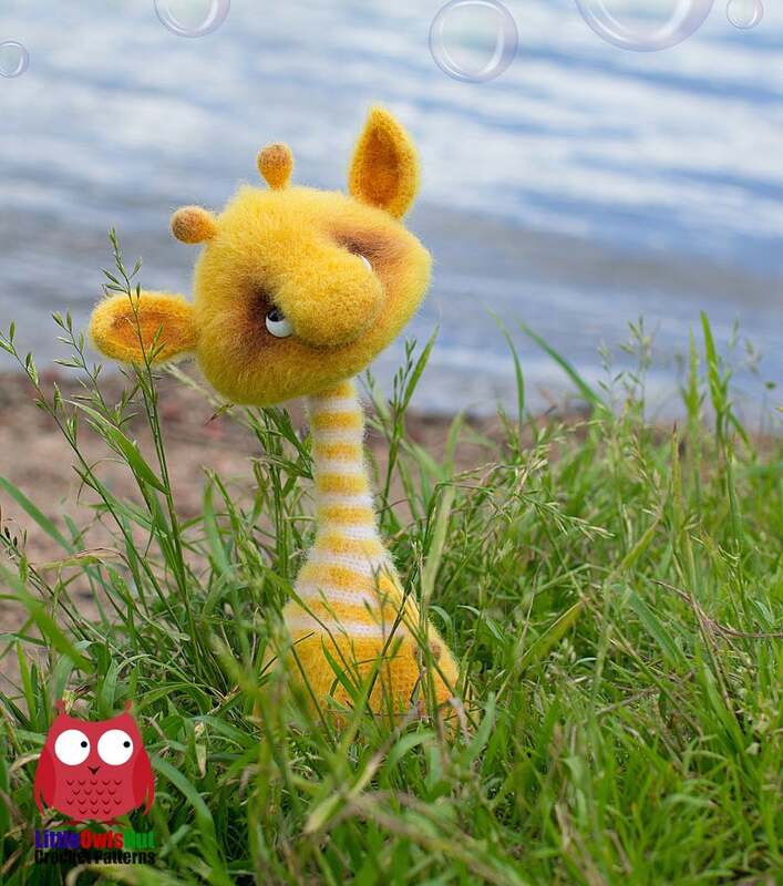 Yellow and white striped crocheted giraffe amigurumi peeking from grass with water and bubbles behind.
