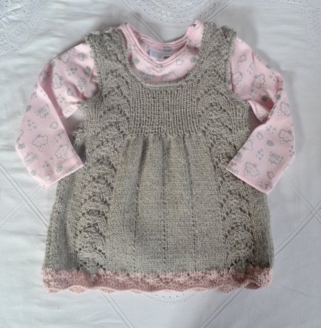 Grau gestricktes Babykleid mit seitlichem Lochmuster und rosa Muschelsaum über rosa Langarmbody
