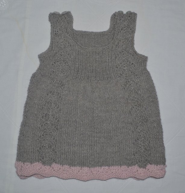 Gestricktes graues Baby- und Kinderkleid, ärmellos, quadratischer Ausschnitt, seitliche Musterstreifen und rosa gewellter Saum