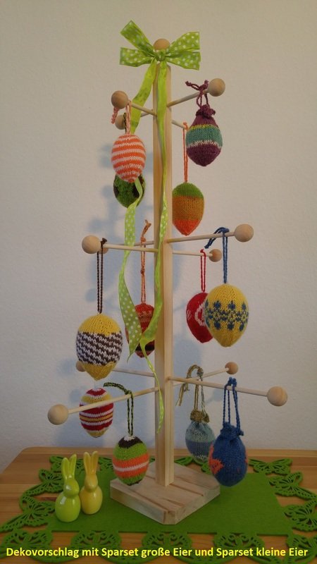 Holzständer mit bunten gestrickten Ostereiern, hellgrüner Schleife und zwei kleinen Hasenfiguren auf grüner Tischmatte