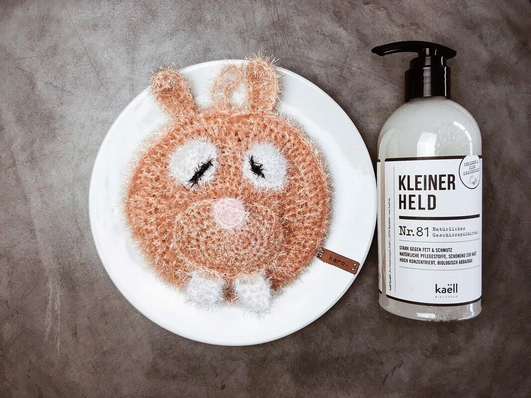 schnell gehäkeltes rundes Küchenpad in Hasenform auf weißem Teller neben Seifenspender