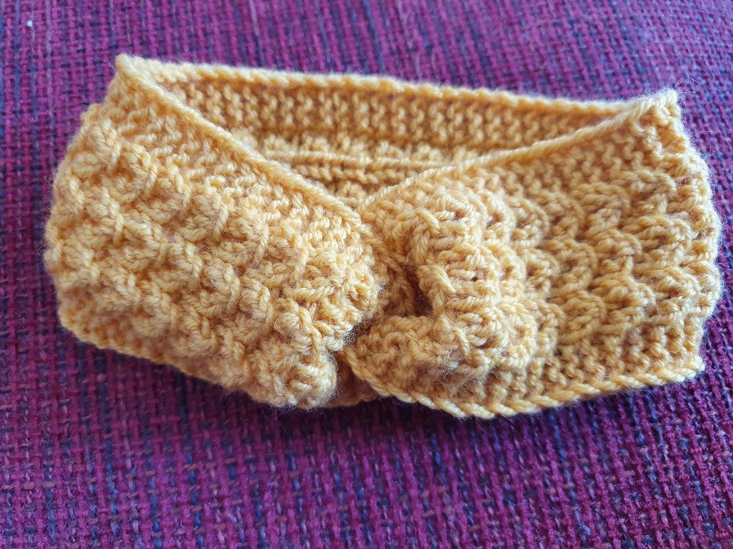 Gestricktes senfgelbes Baby-Stirnband mit Knoten auf violettem Stoff