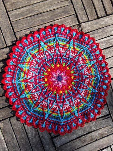 Multicolor crocheted mandala doily with scalloped edge on wooden background
