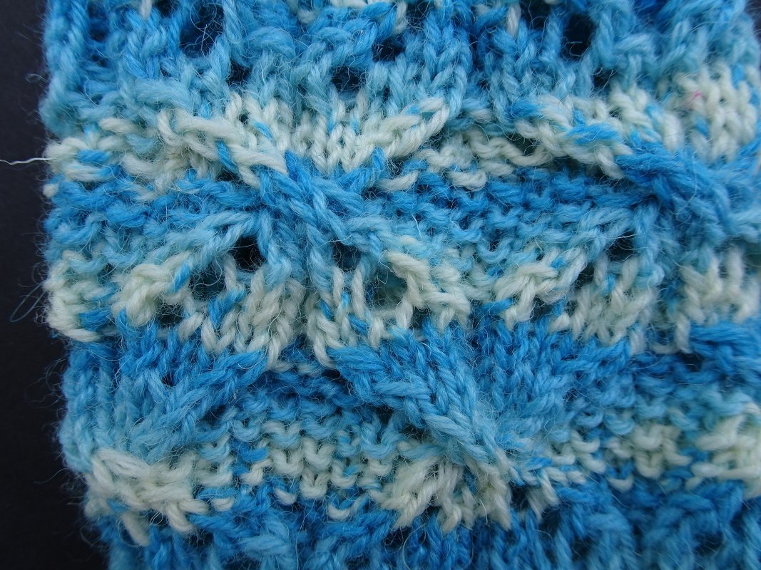 Nahaufnahme eines blau-weißen Strickmusters mit Loch- und Zopfmaschen