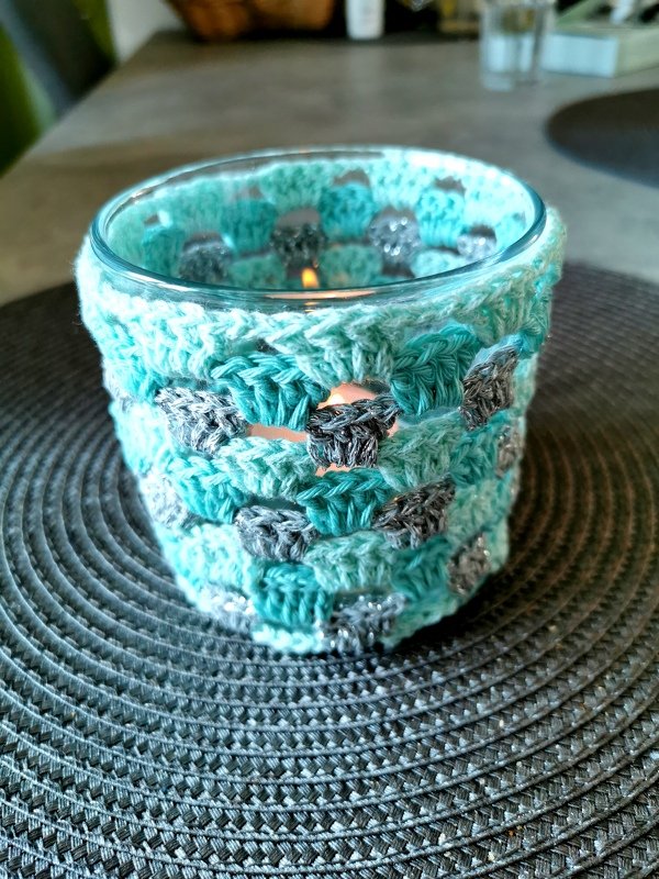 Glas-Teelichthalter mit gehäkelter Hülle in Türkis und Grau, brennende Kerze