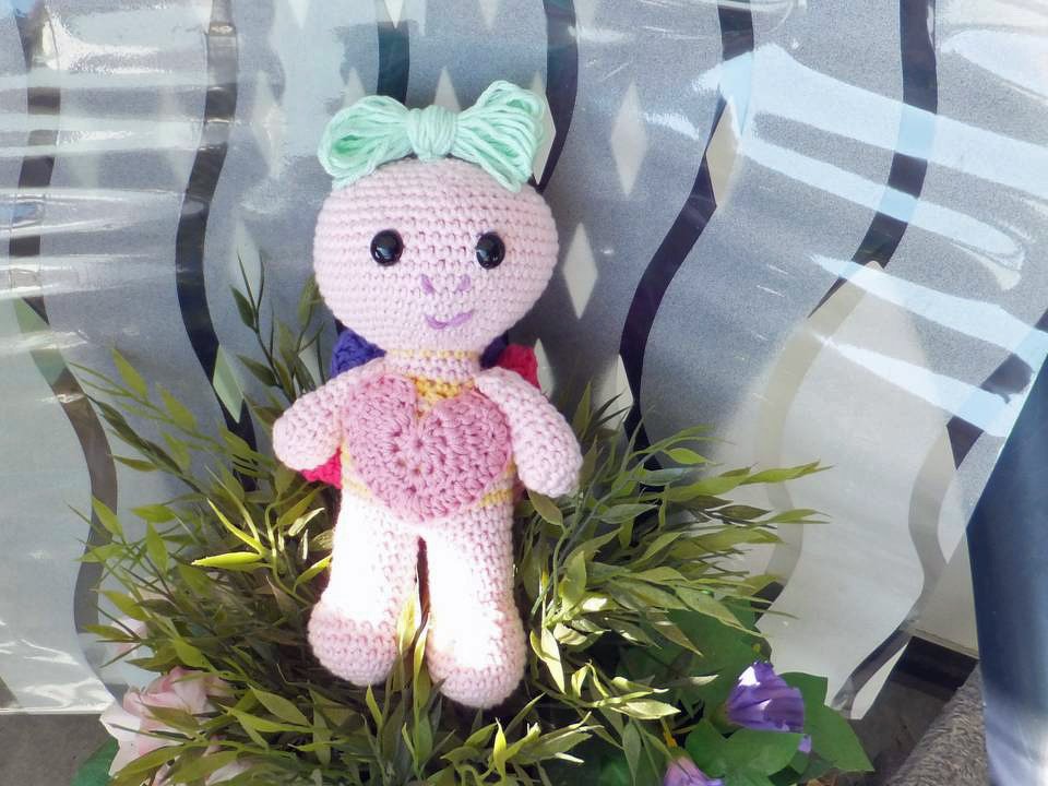 Pastellfarbene gehäkelte Amigurumi-Puppe mit Herzapplikation und grüner Schleife