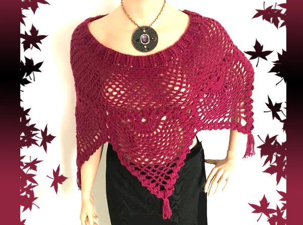 Beerenfarbener gehäkelter Poncho mit durchbrochenem Ajourmuster und Quasten auf einer Schaufensterpuppe.