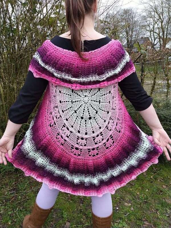 Person von hinten in einer pink-lila gehäkelten Weste mit rundem Mandala-Muster am Rücken und Rüschensaum.
