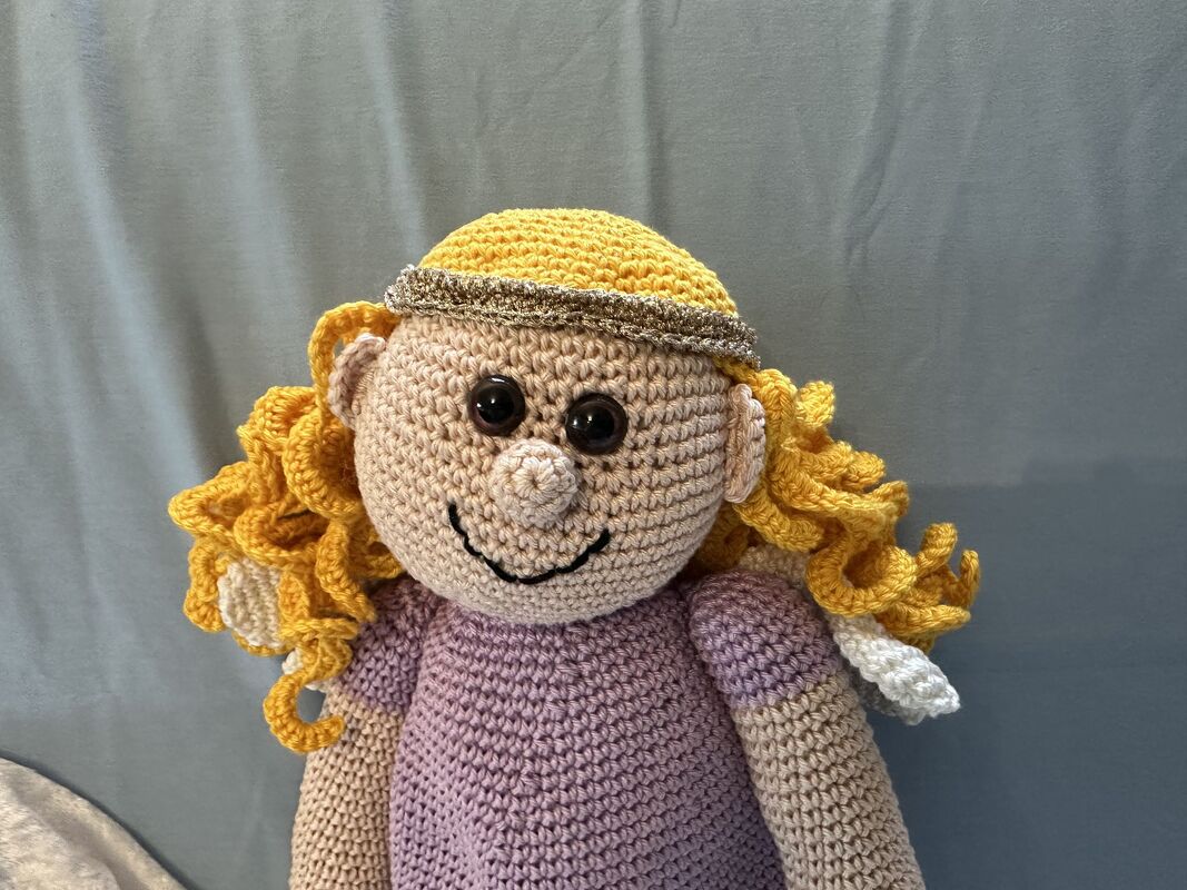 Gehäkeltes Amigurumi‑Engelchen mit gelben Locken, lila Kleid, goldfarbenem Haarschmuck und weißen Flügeln