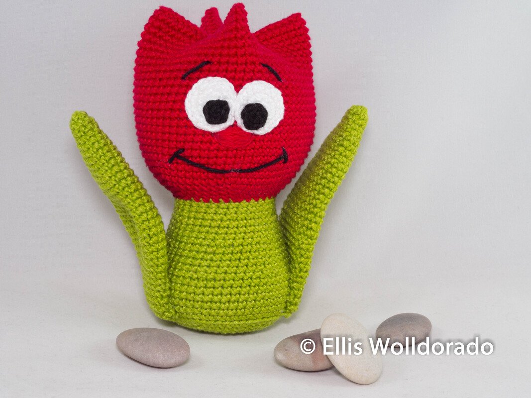 Gehäkelte Tulpe mit rotem Blütenkopf und grünem Körper, sitzend vor hellem Hintergrund