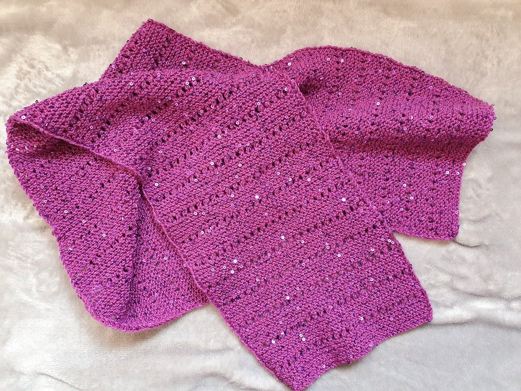 Magentafarbener gestrickter Schal mit kleinen silbernen Pailletten auf hellem Untergrund