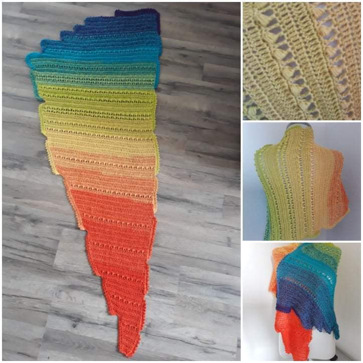 Mehrfarbiges, asymmetrisches gehäkeltes Dreieckstuch mit Regenbogen-Farbverlauf und gestuften gezackten Kanten, teils flach auf Holzboden, teils an einer Puppe drapiert.