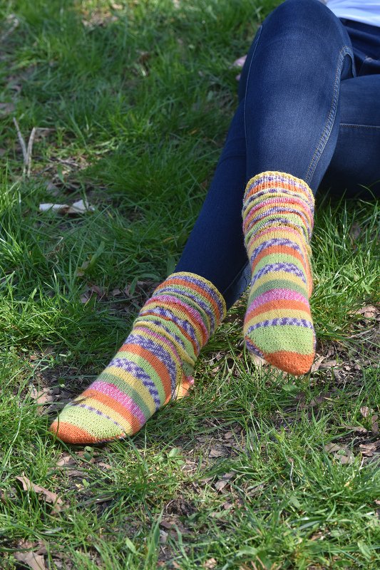 Beine in Jeans mit bunten gestrickten, gestreiften Socken auf grünem Rasen