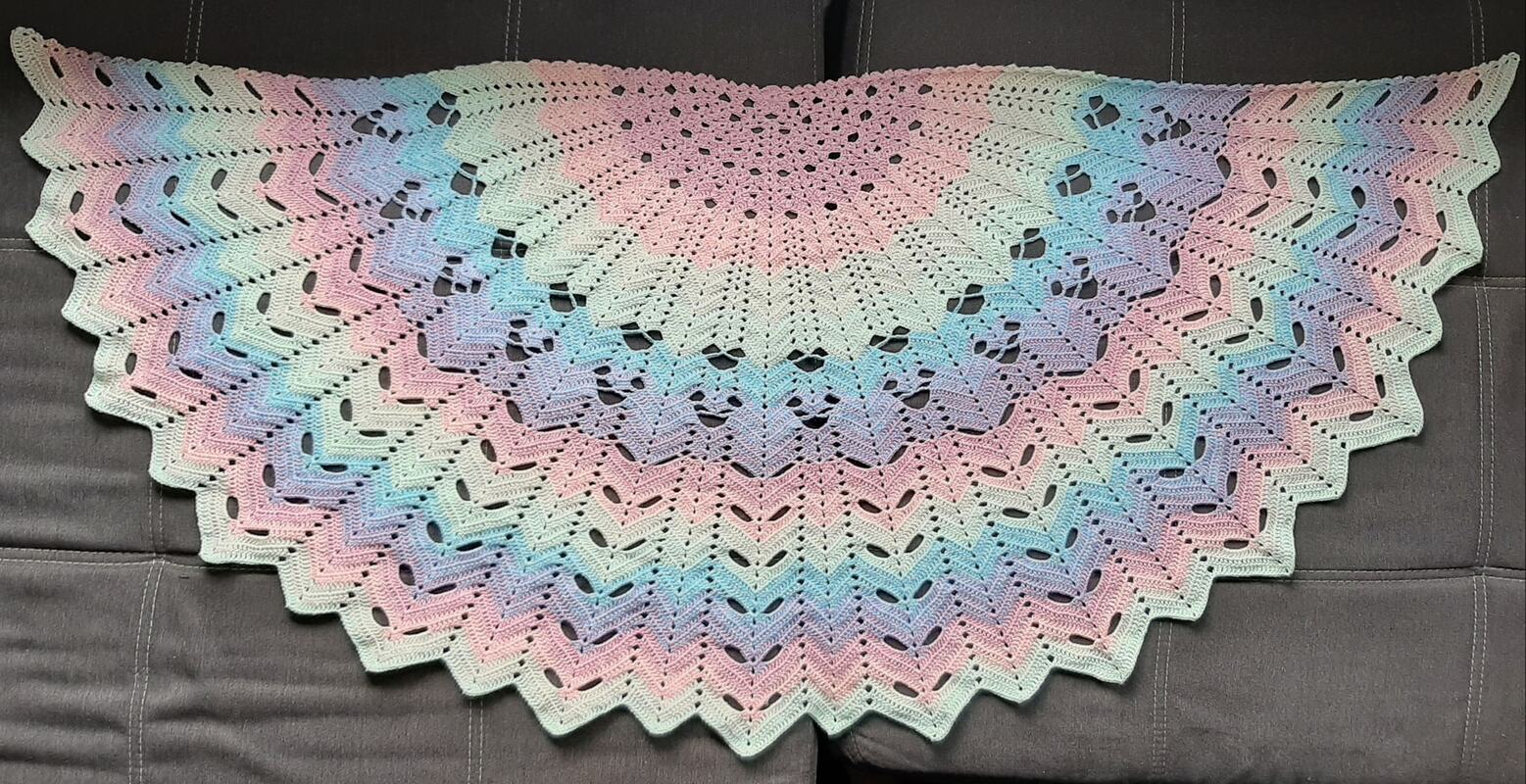 Halbrundes gehäkeltes Tuch in Pastellfarben mit Lochmuster auf dunklem Hintergrund