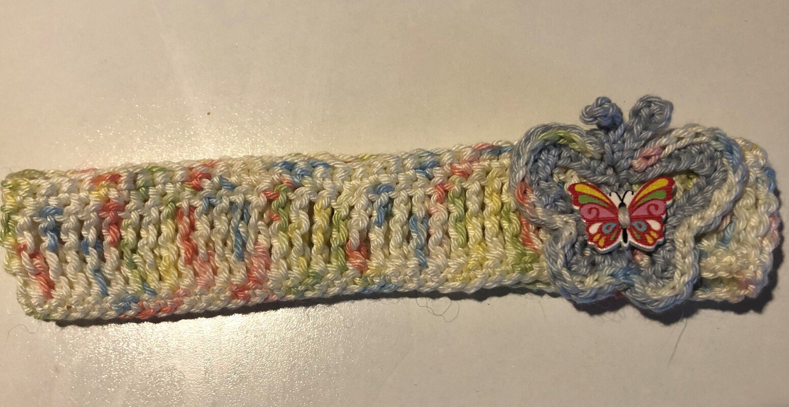 Gehäkeltes Baby-Stirnband in Pastell mit hellblauer Blüten-Applikation und buntem Schmetterlingsknopf