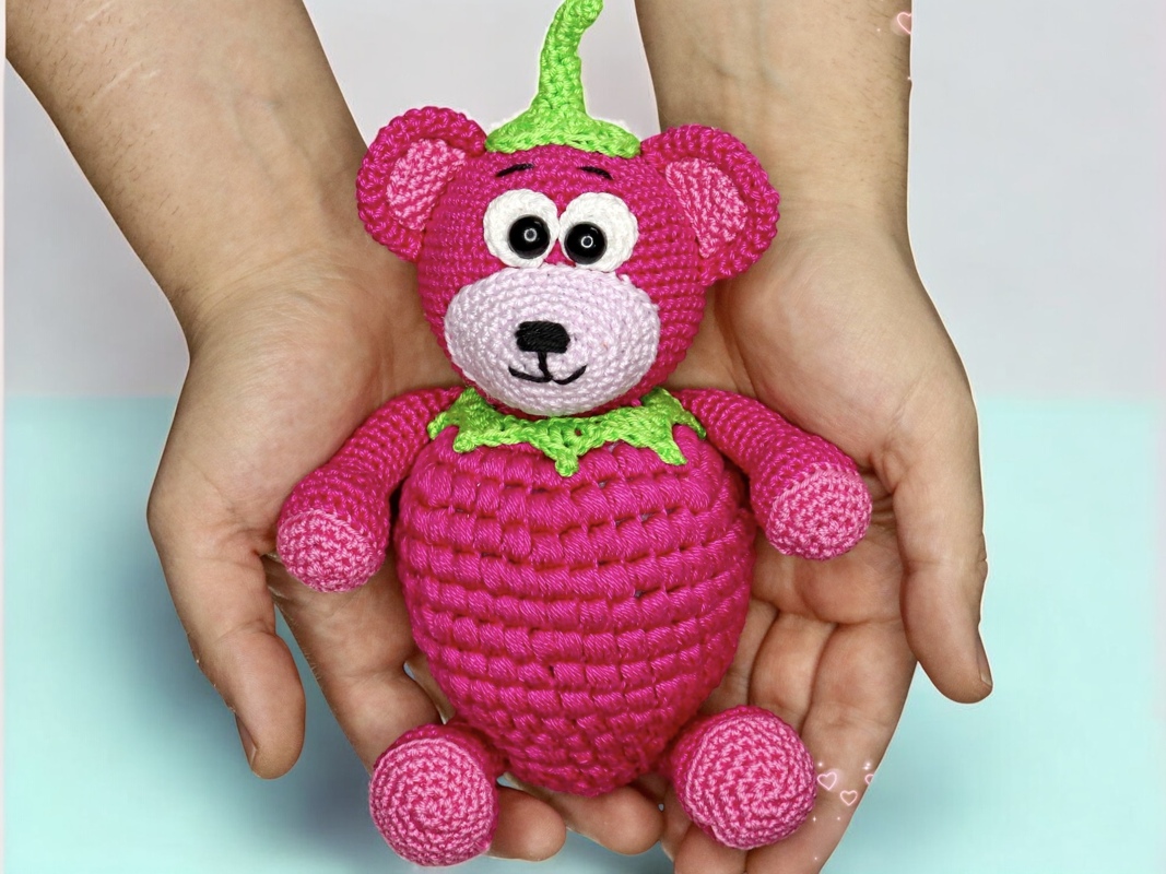 Hand hält gehäkelten pinken Amigurumi-Teddy mit grüner Blattkrone
