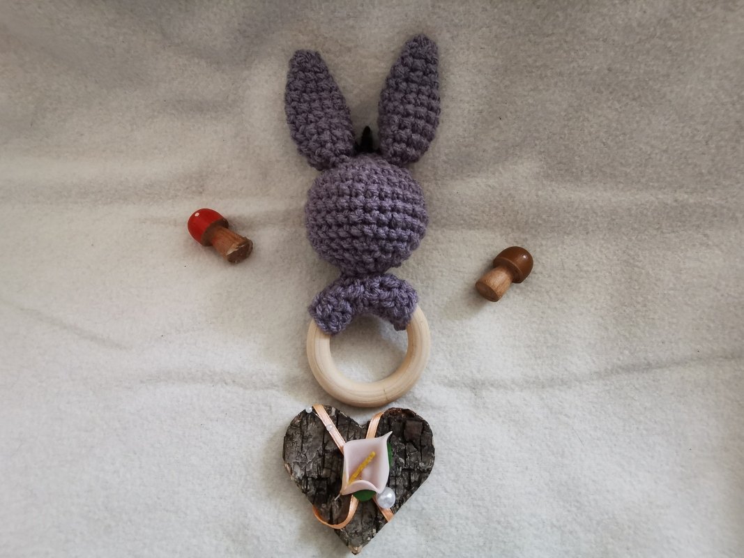 Fliederfarbenes gehäkeltes Häschen auf Holzring mit Holzpilzen und Rindenherz als Geschenkarrangement