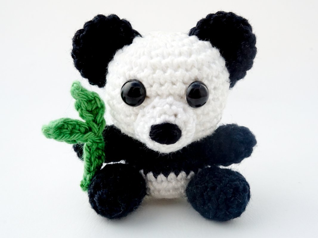 Black-and-white crocheted panda amigurumi holding a small green bamboo leaf on a white background.