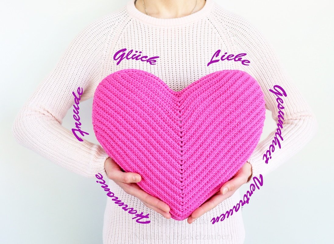 Hands holding a large pink crocheted heart pillow with diagonal textured stitches.